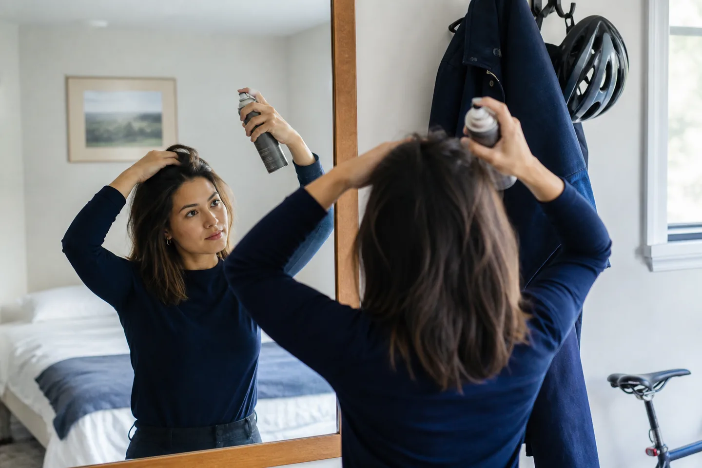Commuter refreshing second-day hair with an unbranded dry shampoo at a bedroom mirror