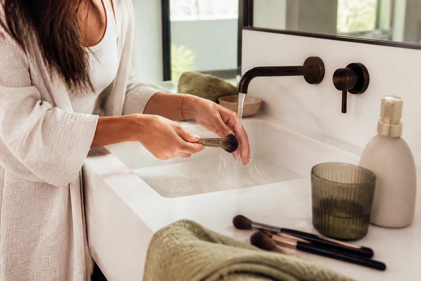 Beauty enthusiast washing a small set of makeup brushes at a bright bathroom sink