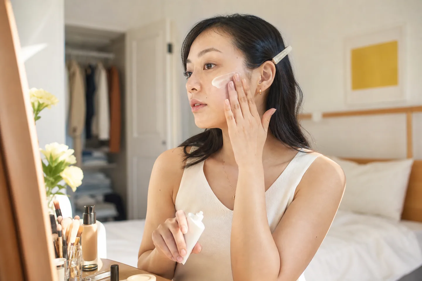 Woman applying facial sunscreen before makeup at a sunny bedroom mirror